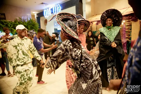 A guest in green and white adire dances in the hall.