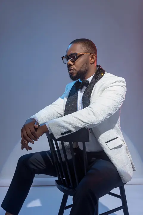 A model in a white tuxedo jacket sits on a chair, lit in cool blue.