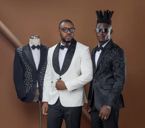 Two men side by side in a white shawl-collar tuxedo and a black embellished jacket.