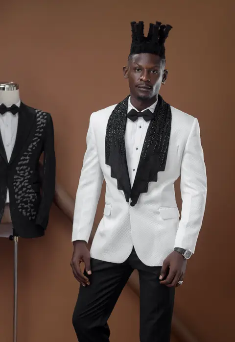A model in a white jacket with a black shawl collar, against a brown studio backdrop.