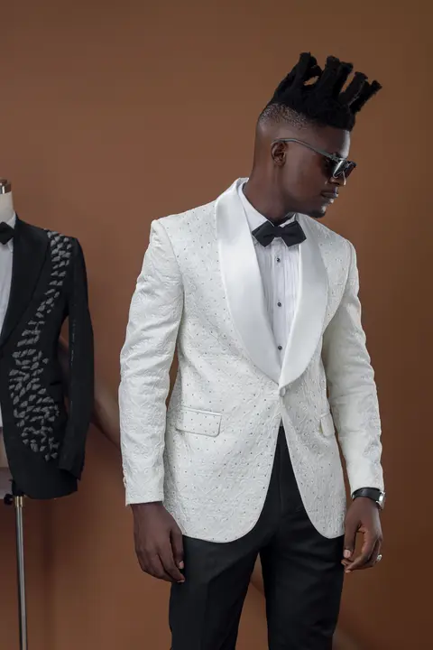A model in a white brocade dinner jacket, hands at his lapels.