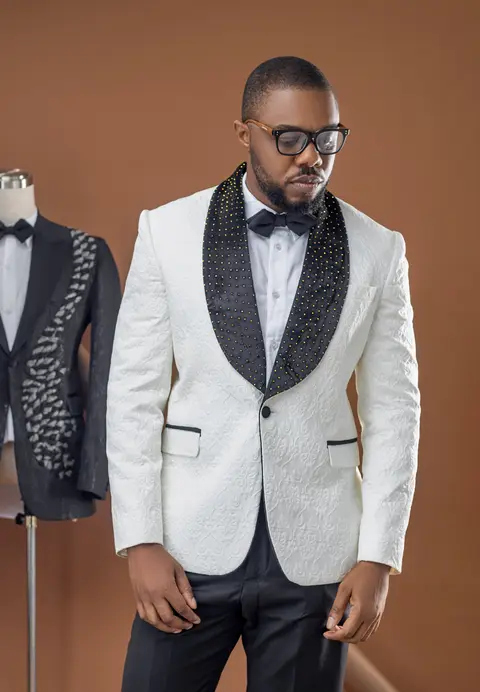 A man in glasses wears a white jacket with a black embroidered shawl collar.