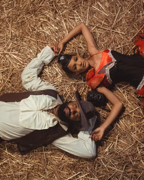 A man and a woman in vintage styling lie head to head on a bed of straw.