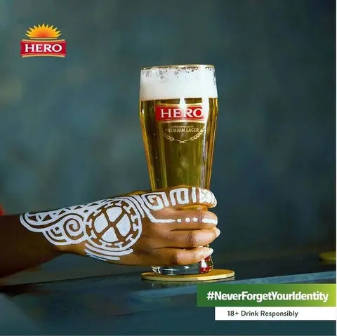 A hand painted with white patterns holds a glass of Hero Lager.