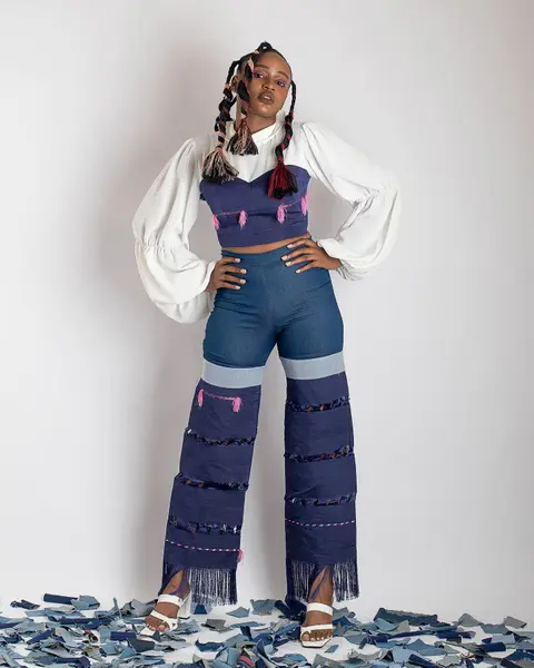 A model with braided hair in a patchwork denim top and wide trousers on a floor of denim scraps.