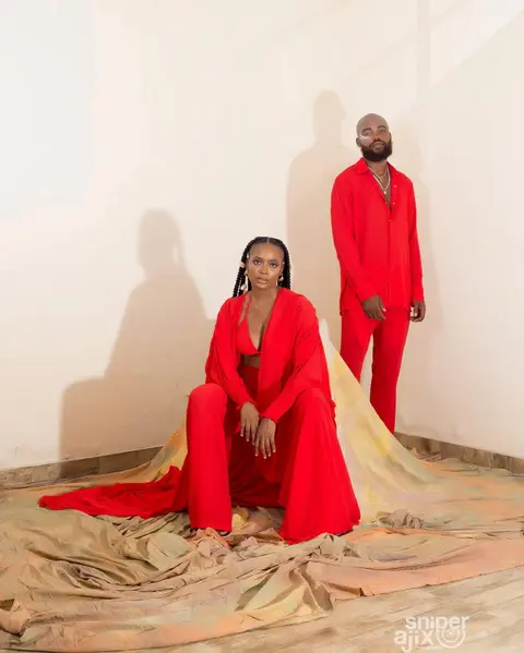 A woman and a man in scarlet tailoring on a painted fabric floor against a cream wall.