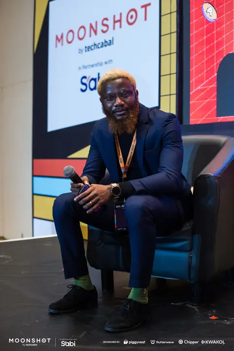 A speaker seated on stage in front of the Moonshot backdrop.
