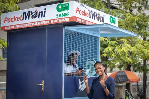 Two agents greet customers at a blue PocketMoni kiosk.
