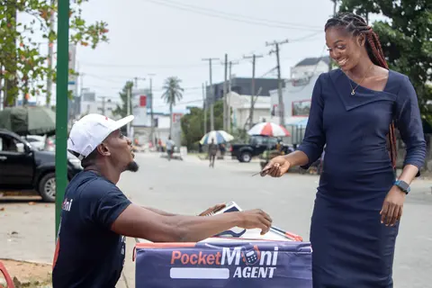 A customer pays a PocketMoni agent at a street-side stand.