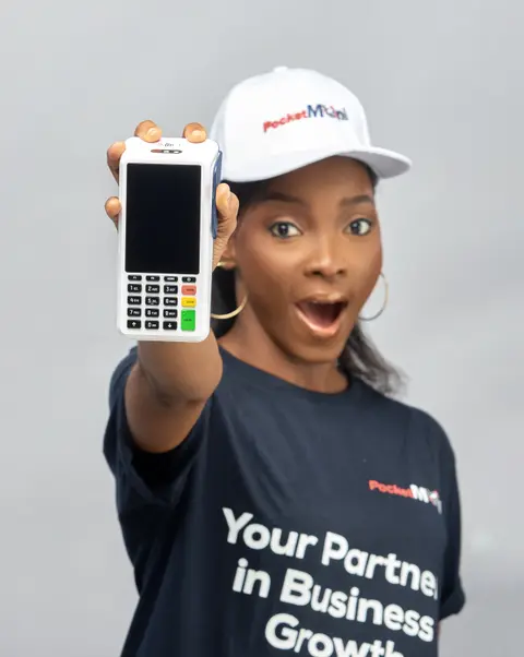 A woman in a PocketMoni cap thrusts a terminal toward the lens, mouth open in surprise.
