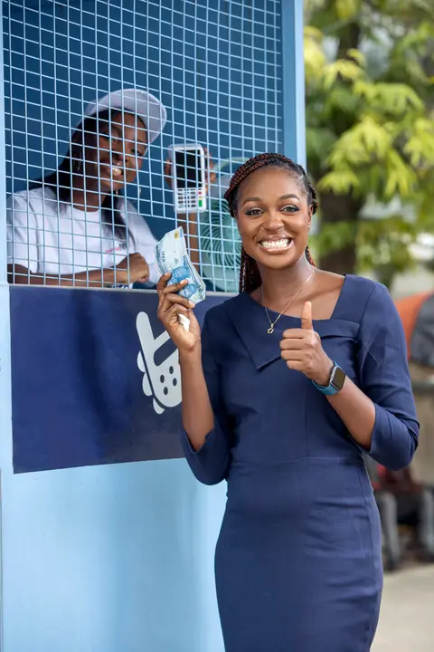 An agent and a customer give a thumbs up at a kiosk window.