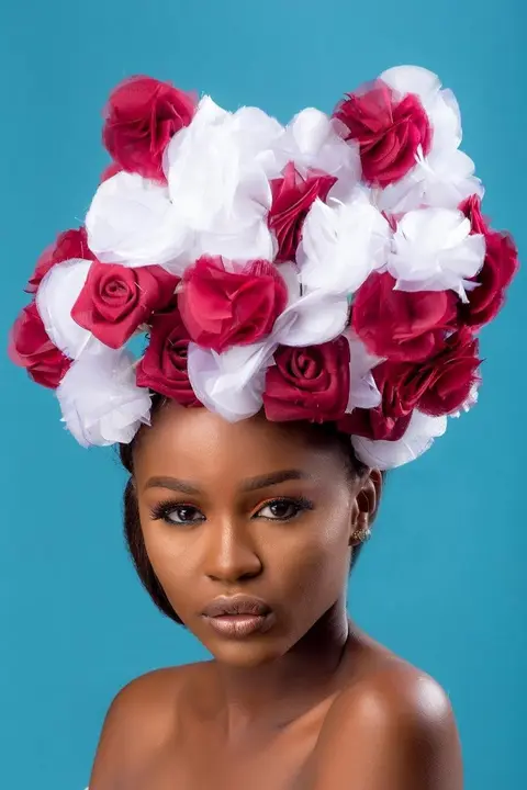 A woman wearing a crown of red and white roses against a teal backdrop.