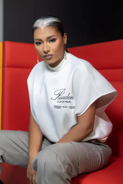A woman with a silver-grey bun in a white oversized tee sits on a red sofa.