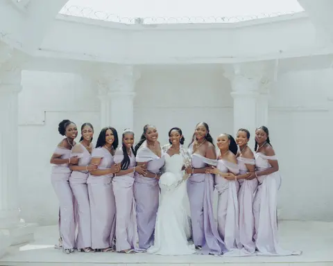 The bride with her bridesmaids in lilac satin under a white rotunda.