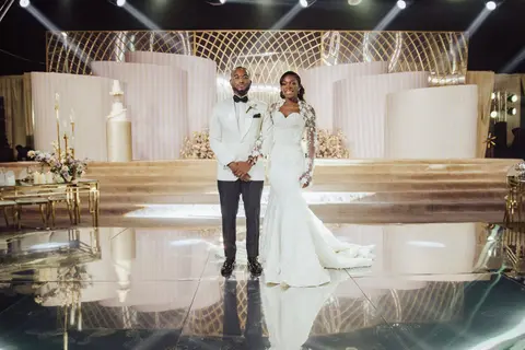 The bride and groom stand on a mirrored dance floor beneath a sculpted white stage set.