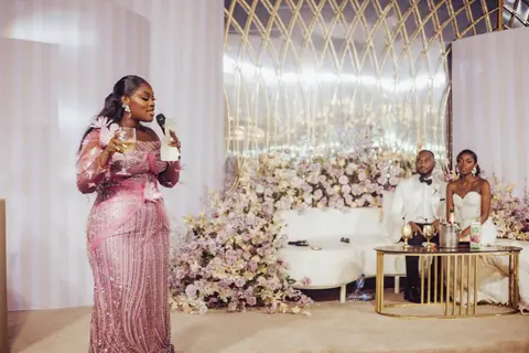 A guest in a pink sequinned gown gives a toast while the couple listen at their floral high table.