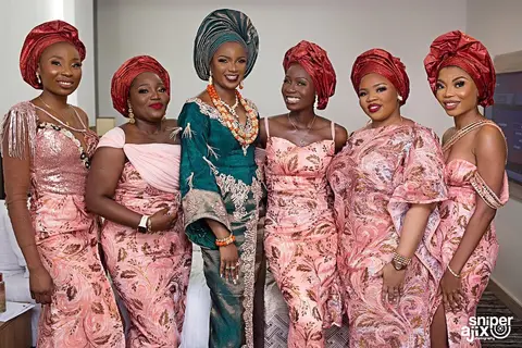 Friends of the bride in matching blush-pink aso-ebi and red gele, laughing together.